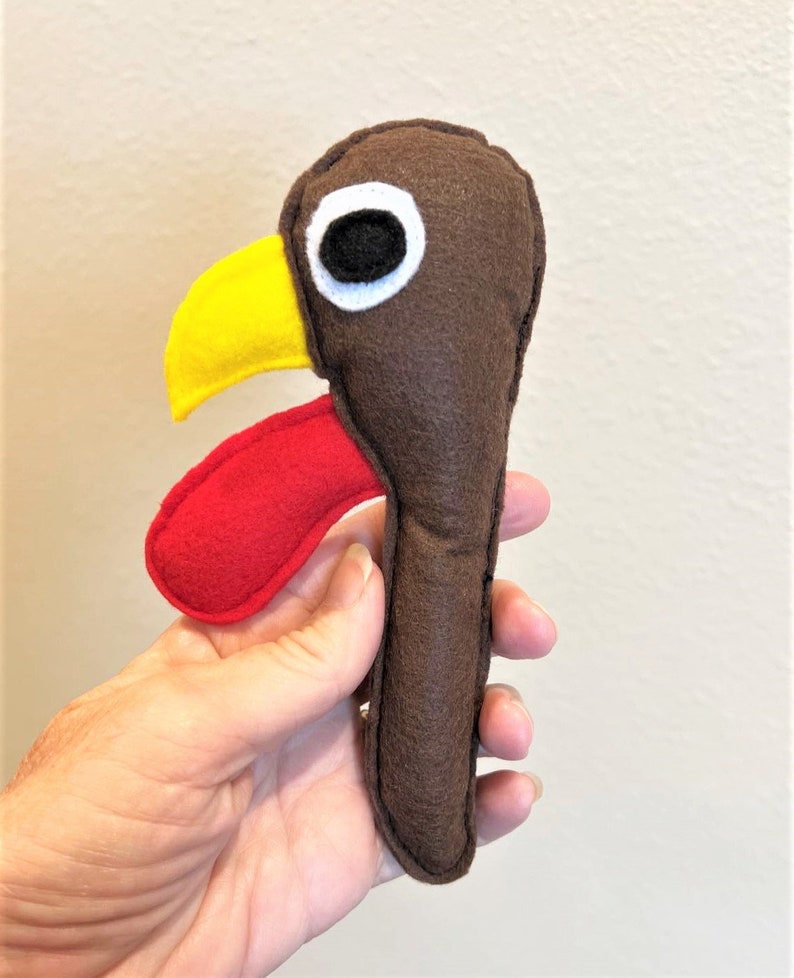 May include: A brown felt turkey puppet with a red wattle, yellow beak, and black eye.
