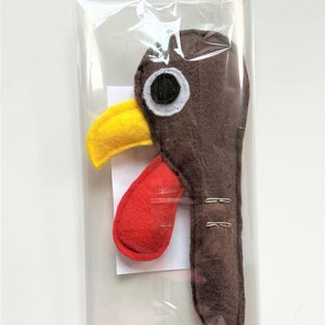 May include: A brown felt turkey head with a yellow beak, red wattle, and a white eye. The turkey head is packaged in a clear plastic bag.