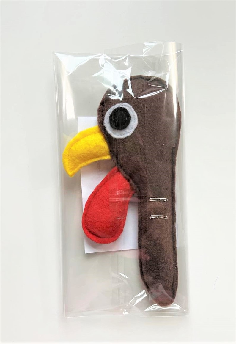 May include: A brown felt turkey head with a yellow beak, red wattle, and a white eye. The turkey head is packaged in a clear plastic bag.