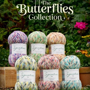 May include: A selection of multi-coloured yarn balls, part of "The Butterflies Collection." The skeins feature various shades like purple, green, and yellow. The yarn is displayed on grass, with a wooden box and foliage in the background. Each ball is labelled.