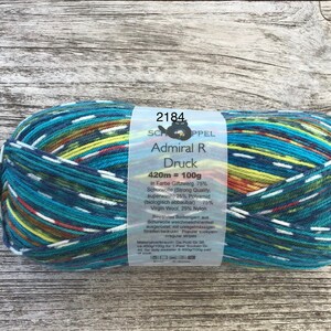 May include: A skein of yarn in the colour "Giftzwerg" with a label that reads "SchoppeL Admiral R Druck 420m = 100g". The yarn is a mix of blue, green, yellow, red, and white stripes.