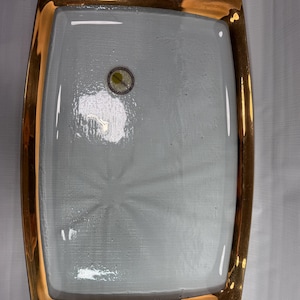 May include: A rectangular glass tray featuring a clear, textured center with a subtle starburst pattern and a wide, reflective metallic gold border. A small circular sticker with the text annieglass is visible on the upper left surface.