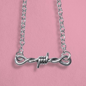May include: A silver necklace with a barbed wire design. The chain is a simple link style.