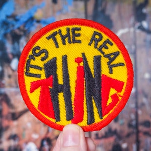 May include: Yellow and red embroidered patch with black text that reads "It's the real thing".