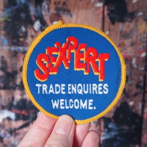 May include: A blue and yellow embroidered patch with the word "Expert" in red lettering and the text "Trade Enquiries Welcome."