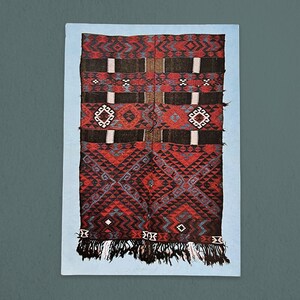 May include: A red, black, and blue woven rug with geometric patterns. The rug has a fringe border.