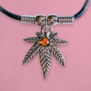 May include: A silver necklace with a black cord and a silver marijuana leaf pendant with an orange gem in the centre.
