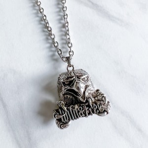 May include: Silver chain necklace with a pendant featuring a detailed eagle head with the words "Wild & Free" inscribed on the pendant.