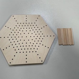 Può includere: Un pannello esagonale in legno con una griglia di fori e un mucchio di pioli in legno.