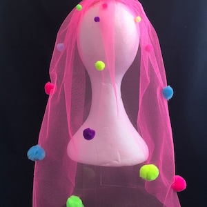 Könnte beinhalten: Rosa Tüll-Schleier mit bunten Bommeln. Der Schleier befindet sich auf einem weißen Mannequin-Kopf.