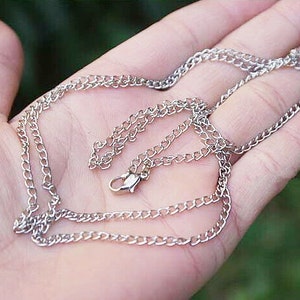 May include: A silver chain necklace with a lobster clasp closure. The chain is made of small, linked metal pieces.