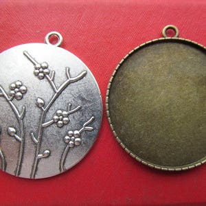 May include: Two silver-toned metal pendants, one with a floral design and the other a blank circle. Both pendants have a loop at the top for hanging.