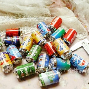 May include: A collection of miniature aluminum beverage cans with various brand logos and designs. The cans are silver with colorful labels and are arranged on a white surface.
