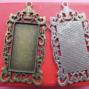 May include: Two ornate metal frames with a rectangular opening. The frame on the left is bronze with a smooth finish. The frame on the right is silver with a textured finish.