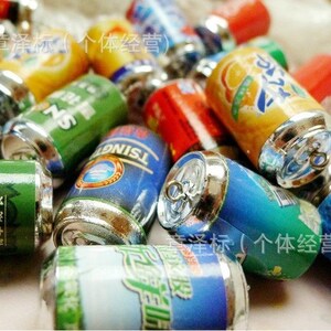 May include: A collection of miniature aluminum beverage cans with various colorful labels and silver tops. The cans feature Chinese text and logos. The cans are arranged in a pile on a table.