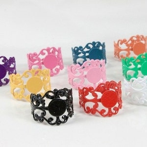 Peut inclure: Assortiment de dix bagues en métal coloré avec un motif de filigrane. Chaque bague a un espace rond vide au centre.
