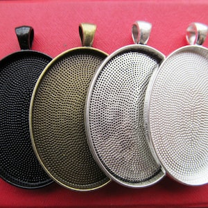 Może przedstawiać: Cztery okrągłe metalowe tacki do zawieszek w kolorze czarnym, brązowym, srebrnym i białym. Każda tacka ma fakturowaną powierzchnię i pętlę u góry do zawieszenia.