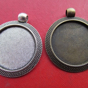 Puede incluir: Dos bandejas redondas de metal para colgantes con un borde decorativo. La bandeja de la izquierda es plateada y la de la derecha es bronce.