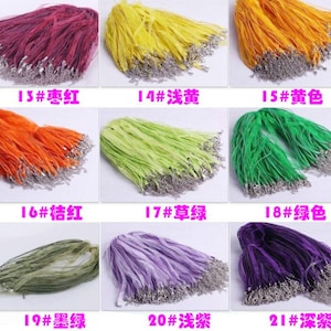 Könnte beinhalten: Eine Sammlung von 10 verschiedenen Farben von Band, jede Farbe ist gebündelt. Das Band ist ein dünnes, durchsichtiges Material. Jedes Bündel hat einen silbernen Metallverschluss am Ende des Bandes.