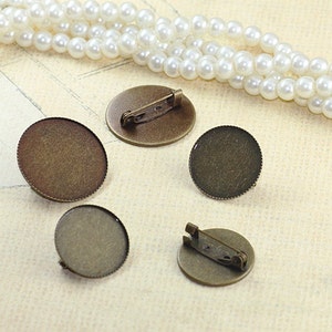 May include: Four round, antique gold-toned metal blanks with a beveled edge. Two of the blanks have a pin back attached. These blanks are perfect for creating custom jewelry.