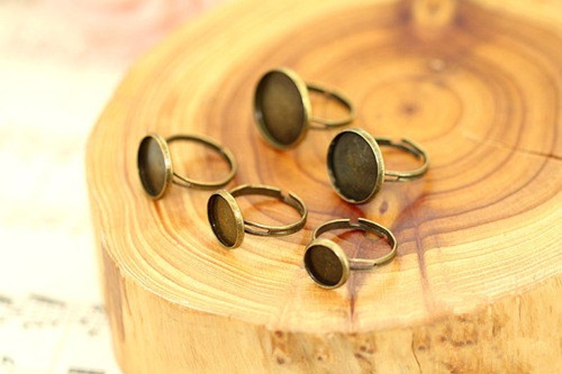 May include: Five bronze-coloured rings with round glass inserts. The rings are on a wooden surface.