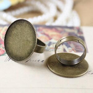 May include: Two bronze ring blanks with a round, flat surface. The ring blanks are ready to be customized with resin, paint, or other embellishments.