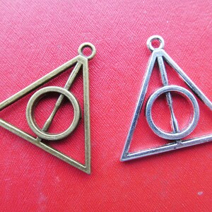 May include: Two triangle-shaped charms with a circle inside. One charm is silver and the other is gold.