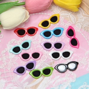 May include: Assortment of colourful plastic sunglasses with different coloured frames and lenses. The sunglasses are arranged on a white lace background.