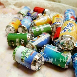 May include: A collection of miniature aluminum cans with various colorful designs and labels. The cans have silver tops and bottoms. The text on the cans reads "SN" and "章泽标(个体经营)".