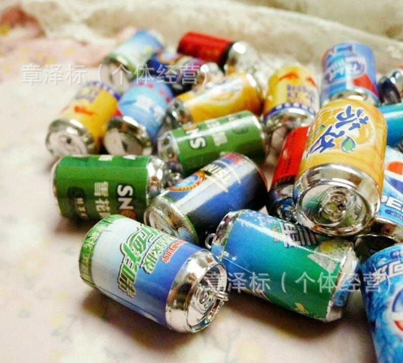 May include: A collection of miniature aluminum cans with various colorful designs and labels. The cans have silver tops and bottoms. The text on the cans reads "SN" and "章泽标(个体经营)".