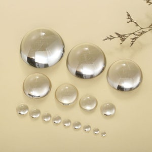 May include: A set of clear glass cabochons of various sizes. The cabochons are round and smooth, with a polished finish. They are arranged in a row, from largest to smallest.