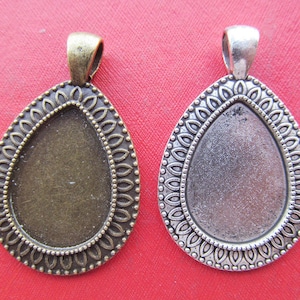 Könnte beinhalten: Zwei ovale Metall-Anhänger-Tabletts mit dekorativem Rand. Das Tablett links ist bronzefarben und das Tablett rechts ist silberfarben.