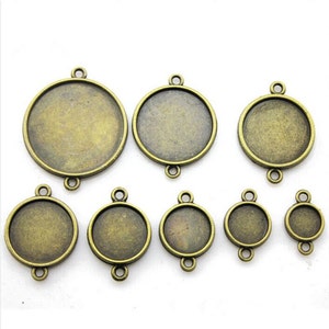 May include: Assortment of eight round metal pendant trays in various sizes. The trays are antique gold in color and have three loops on the top for attaching to a chain or cord.