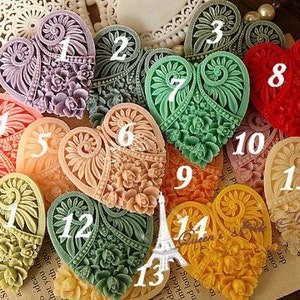 Könnte beinhalten: Fünfzehn herzförmige Harz-Ornamente mit aufwendigen Blumendesigns in verschiedenen Farben, darunter Rosa, Grün, Rot und Creme. Jedes Herz ist von 1 bis 15 nummeriert.
