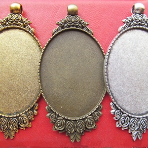 Puede incluir: Tres marcos de fotos ovalados de metal con diseños florales ornamentados. Los marcos son de oro, bronce y plata.