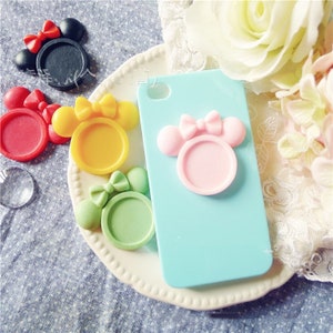Puede incluir: Una funda de teléfono azul claro con un diseño rosa inspirado en Minnie Mouse. La funda presenta un marco redondo con dos orejas redondas y un lazo. También se ven otros marcos coloridos inspirados en Minnie Mouse en rojo, amarillo, verde y negro.