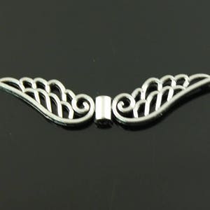 May include: Silver-toned metal angel wing charm with a delicate, openwork design. The wings are connected by a small, cylindrical spacer.