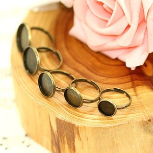 May include: Six antique gold-toned ring blanks with round glass cabochons. The ring blanks are arranged on a wooden surface.