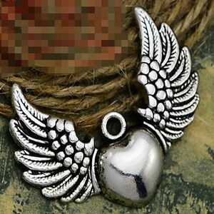 May include: Silver charm with a heart and angel wings. The wings are detailed with small circles and the heart is smooth.
