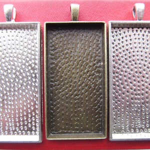 Op de afbeelding: Drie zilverkleurige metalen fotolijsten met een gestructureerd oppervlak. De lijsten hebben een oogje bovenaan om op te hangen.