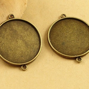 May include: Two round, antique gold-toned metal pendant trays with a smooth, slightly textured surface. Each tray has three loops for attaching a chain or cord.