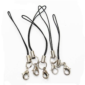 May include: Five black phone straps with silver metal clasps and rings. The straps are made of thin black cord and have a silver metal barrel at the end.