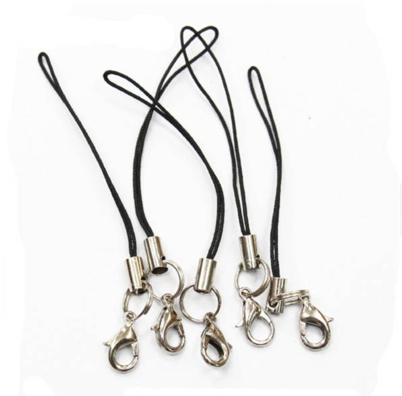 May include: Five black phone straps with silver metal clasps and rings. The straps are made of thin black cord and have a silver metal barrel at the end.