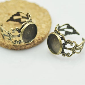 Puede incluir: Dos anillos de estilo antiguo en tono dorado con un diseño de filigrana y un bisel redondo de vidrio transparente. Los anillos son perfectos para agregar un toque vintage a cualquier proyecto de joyería.