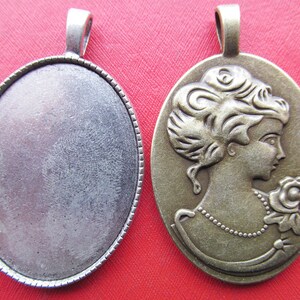 May include: Two oval-shaped metal pendants, one with a blank surface and the other with an embossed image of a woman's profile with a rose.