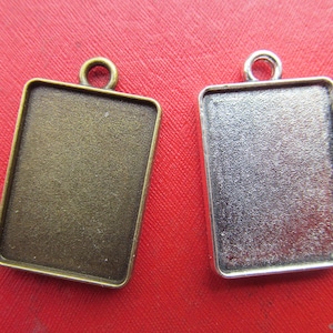 Könnte beinhalten: Zwei Metall-Anhänger-Tabletts, eines silberfarben und eines bronzefarben, mit rechteckiger Form und einer Öse oben zum Aufhängen.