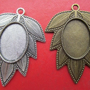 Op de afbeelding: Twee bladvormige hanger-schalen in zilver en brons met een ronde, ovale lege ruimte in het midden. De schalen zijn perfect om een ​​persoonlijke touch toe te voegen aan het maken van sieraden.