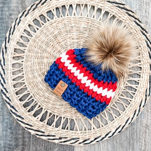 May include: Blue, red, and white striped crocheted beanie with a brown faux fur pom pom. The beanie has a brown leather tag that says "Stitch Fiesta".