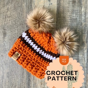 May include: Crochet pattern PDF for a beanie with two brown faux fur pom poms. The beanie is orange, brown, and white striped. The pattern is from Stitch Fiesta.
