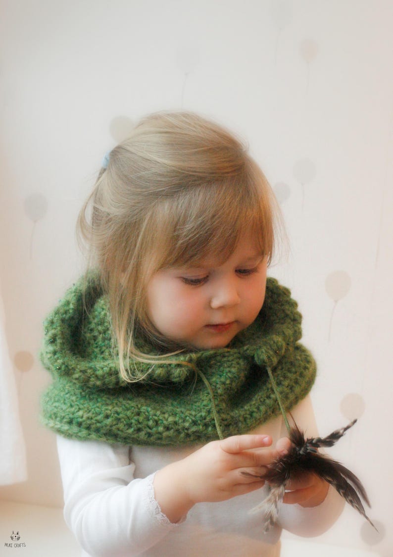 Peut inclure: Un enfant portant un cache-cou vert tricot&eacute;, tenant une plume sombre. L'arri&egrave;re-plan est de couleur claire avec un motif de cercles blancs. L'enfant porte une chemise blanche &agrave; manches longues.